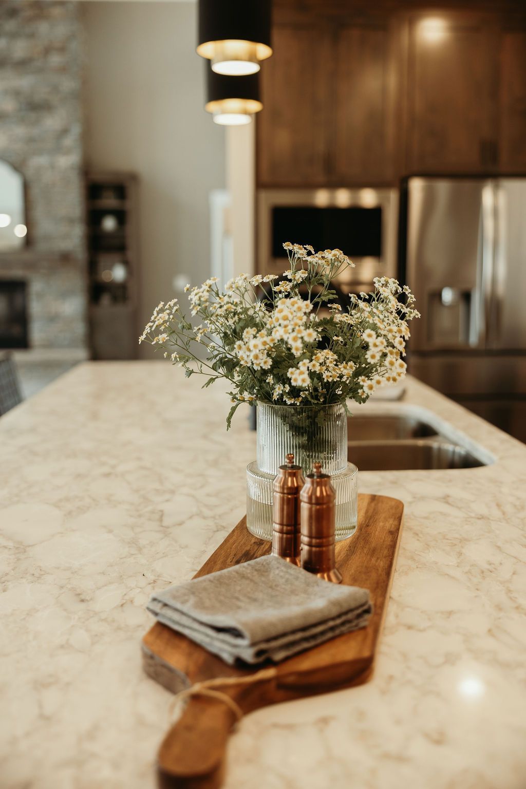 A kitchen island with a wood cutting board holding flowers, salt/pepper shakers, and a linen towel.