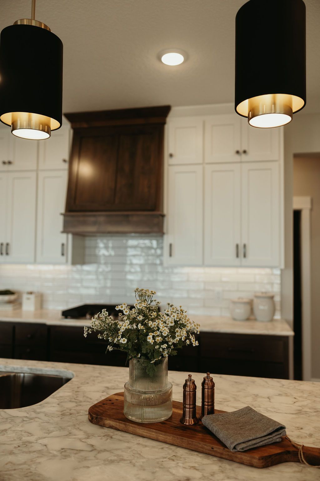 Kitchen with white cabinets, dark hood and countertops. Black pendant lights and vase of flowers on island.