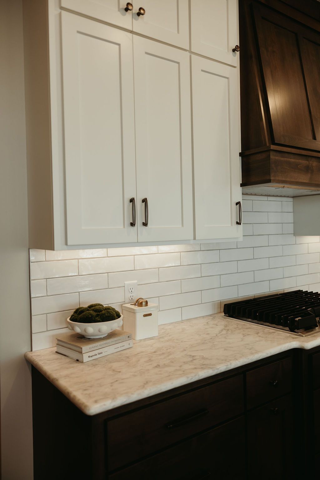 White kitchen cabinets with dark hardware and dark lower cabinets, white tiled backsplash.