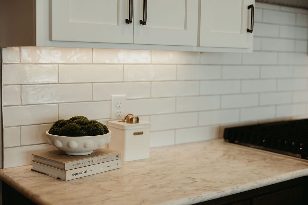 Kitchen with white cabinets, subway tile backsplash, and marble countertops; a plant and container sit on the counter.