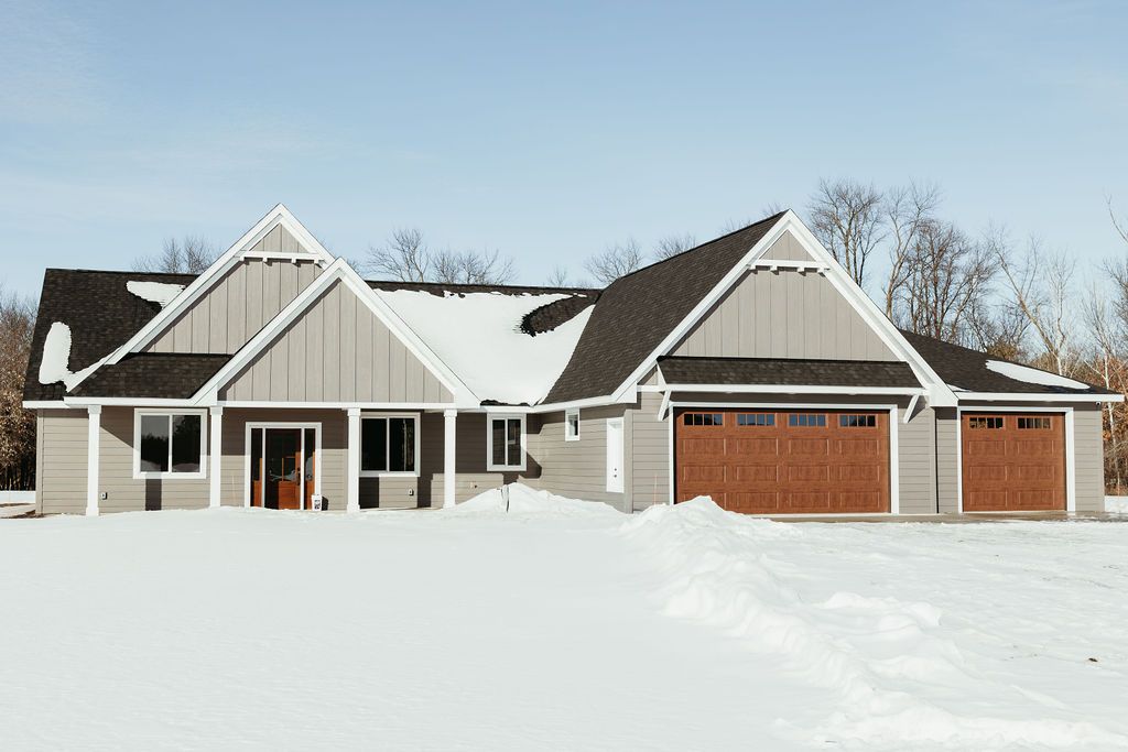 Gray house with brown garage doors, covered in snow, against a blue sky.