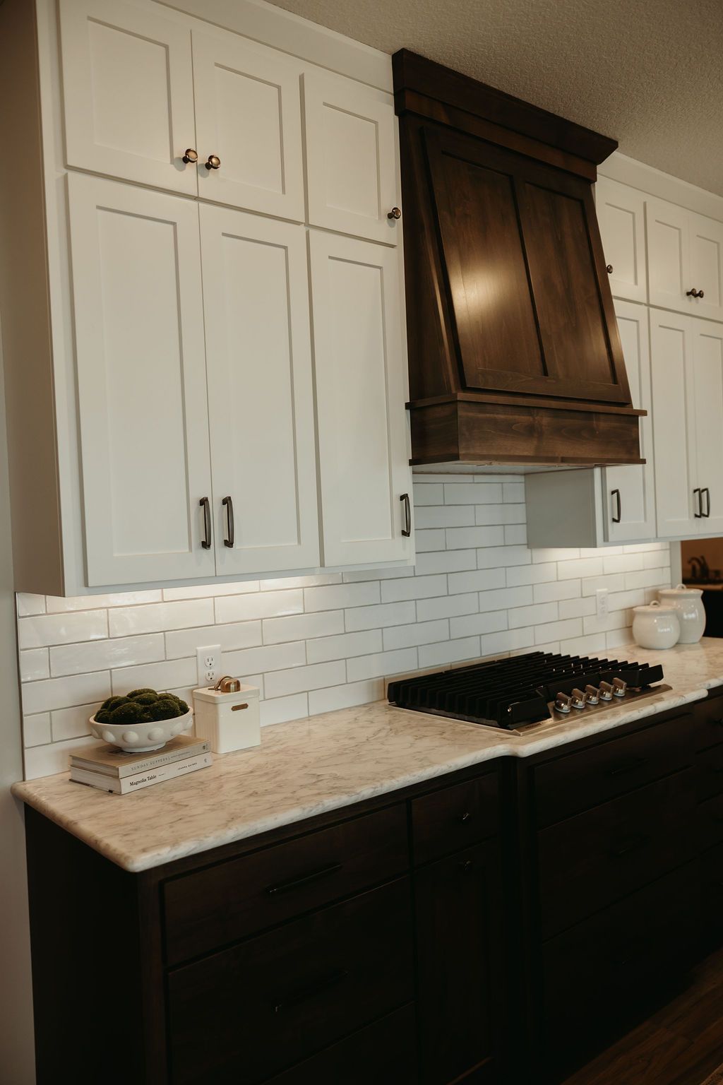 Kitchen with white upper cabinets, dark lower cabinets, and a dark wooden range hood.