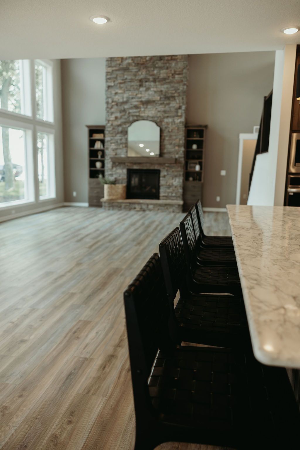 Spacious living room with stone fireplace, built-in shelving, large windows, and a breakfast bar with black stools.