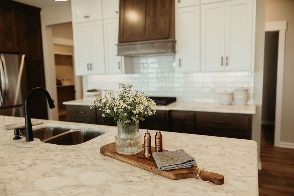 Kitchen with white and brown cabinets, light countertops, and a wooden cutting board with flowers.