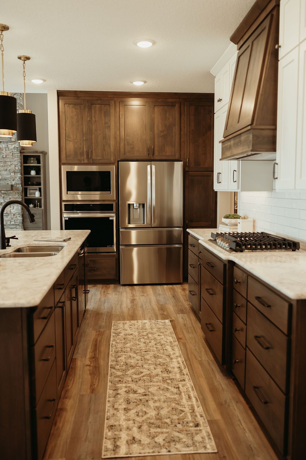 A modern kitchen with dark brown cabinets, stainless steel appliances, and a light-colored runner rug.