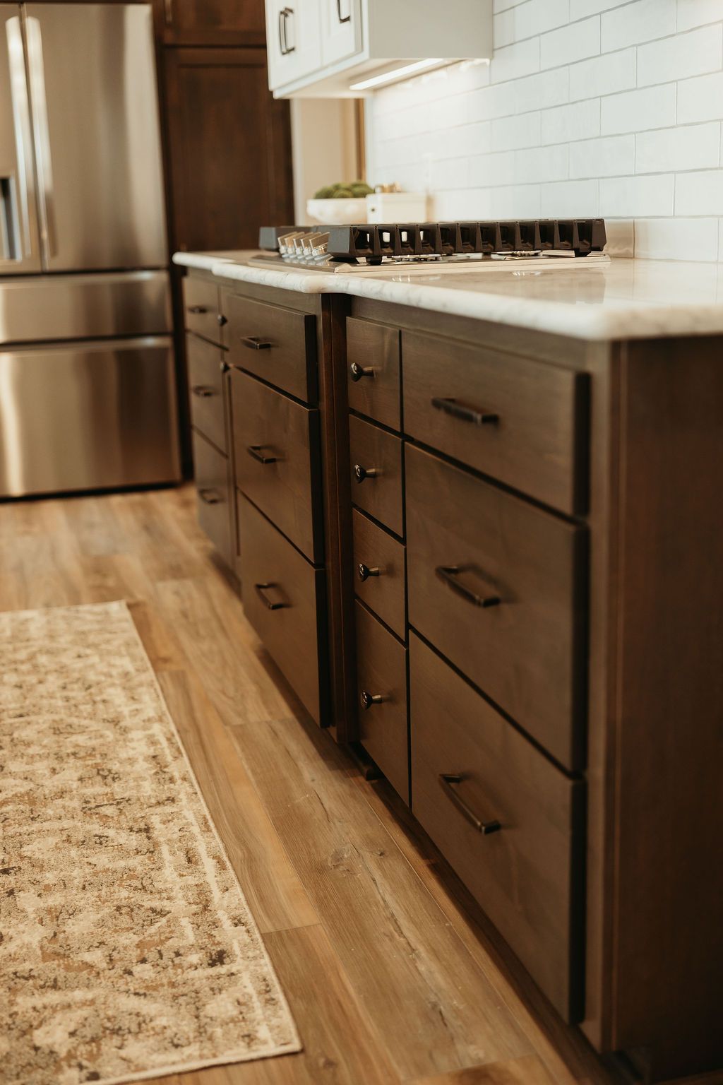 Kitchen with brown cabinets, stainless steel refrigerator, white countertops, and wood floor.