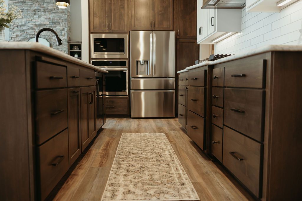 Kitchen with wooden cabinets, stainless steel appliances, and a patterned rug on a light wood floor.