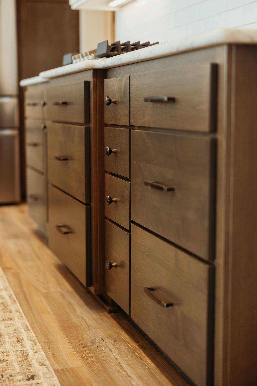 Wooden kitchen cabinets with drawers and black handles, on a light wood floor.