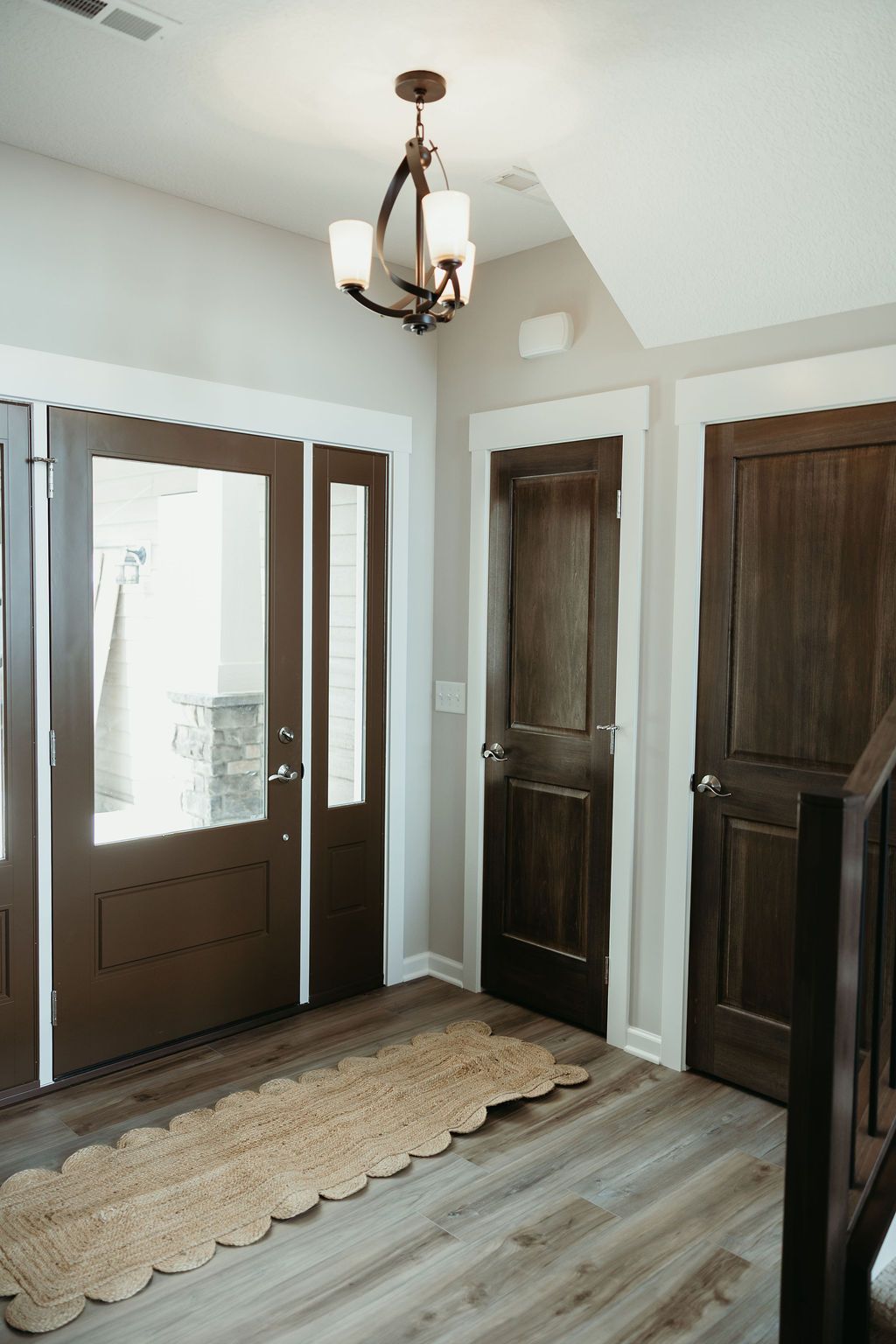 Entryway with brown doors, wood-look flooring, neutral walls, and a decorative light fixture.