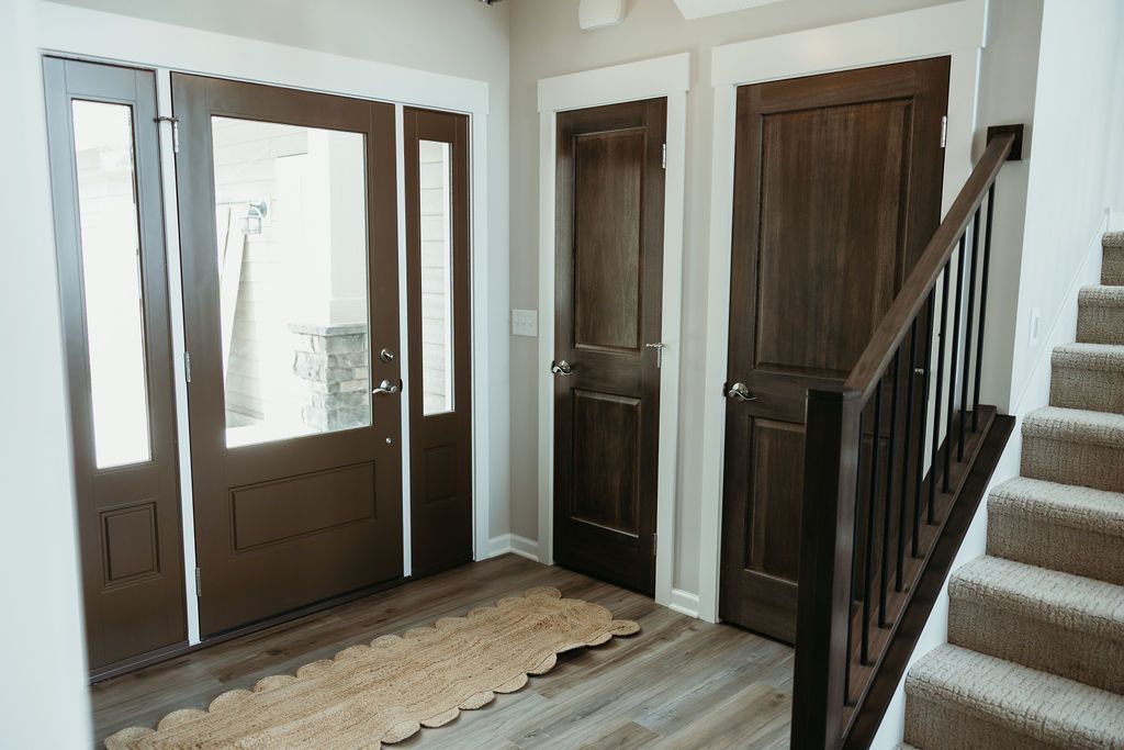 Brown front door with sidelight and two interior doors, entry rug, stairs on the right.