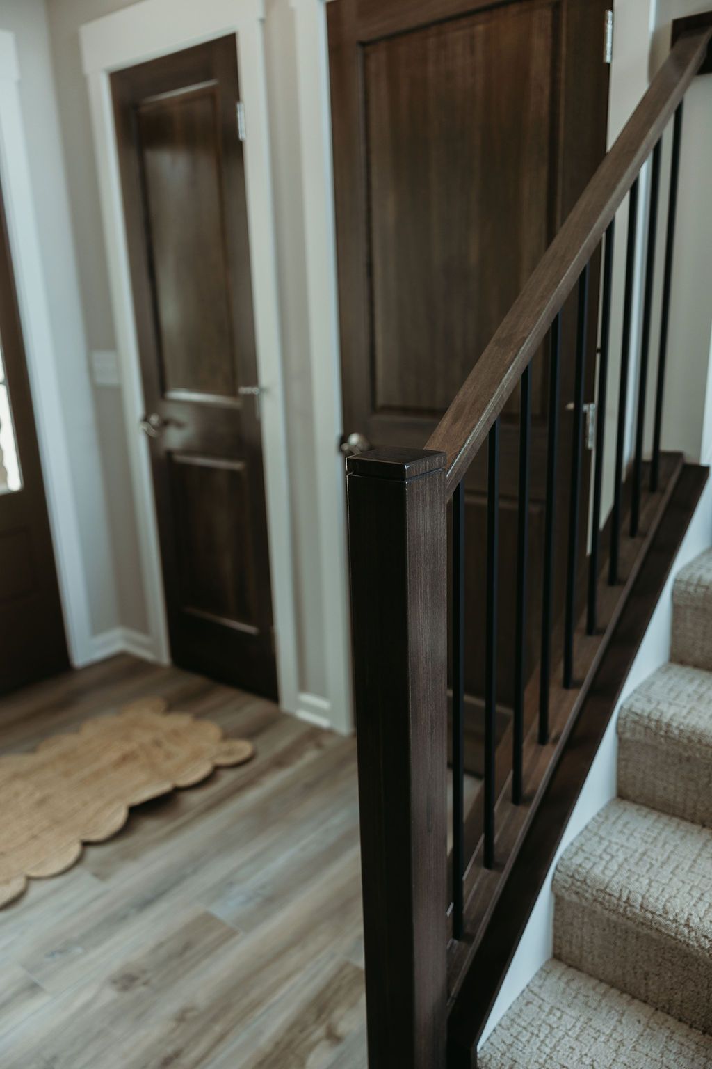Staircase with dark wood banister and black metal spindles. Beige carpeted stairs and wood doors are in the background.