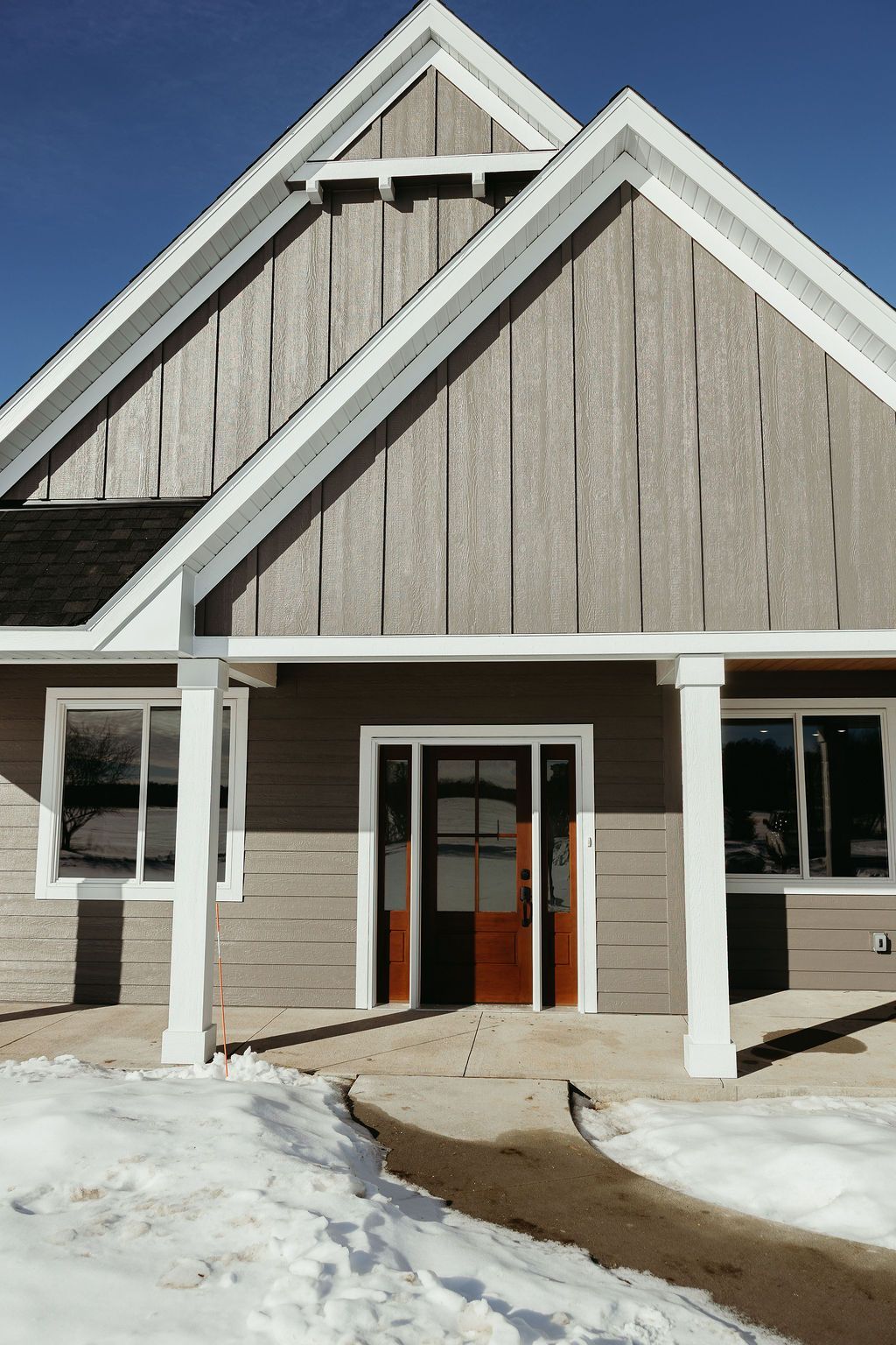 Tan and white building entrance with brown door and porch, snow on ground.