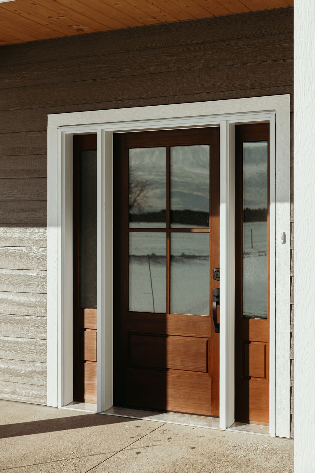 Brown wooden door with glass panels and white trim, set in a gray and white building.