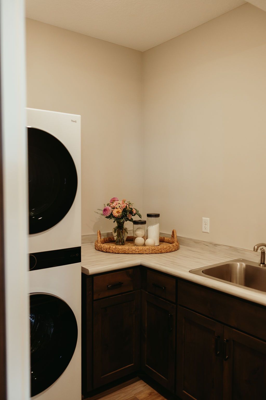 Laundry room with stacked white washer/dryer, dark cabinets, a sink, and a decorative tray.