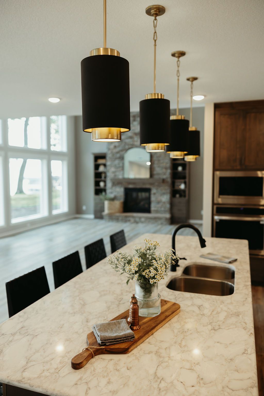 Kitchen with island, black and gold pendant lights, and a fireplace in the background.
