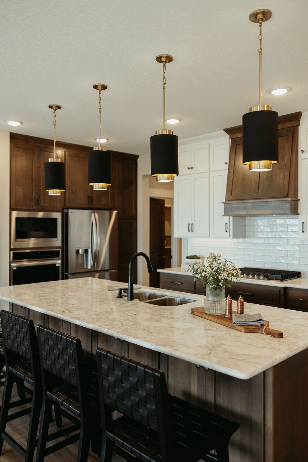 Modern kitchen with island and pendant lights. Black and gold fixtures over a marble countertop and dark wood cabinetry.