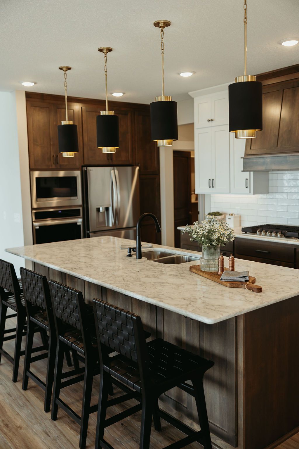 Modern kitchen with island, black pendant lights, and black woven bar stools.