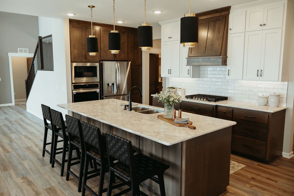 Modern kitchen with a large island, brown and white cabinets, and black pendant lights.
