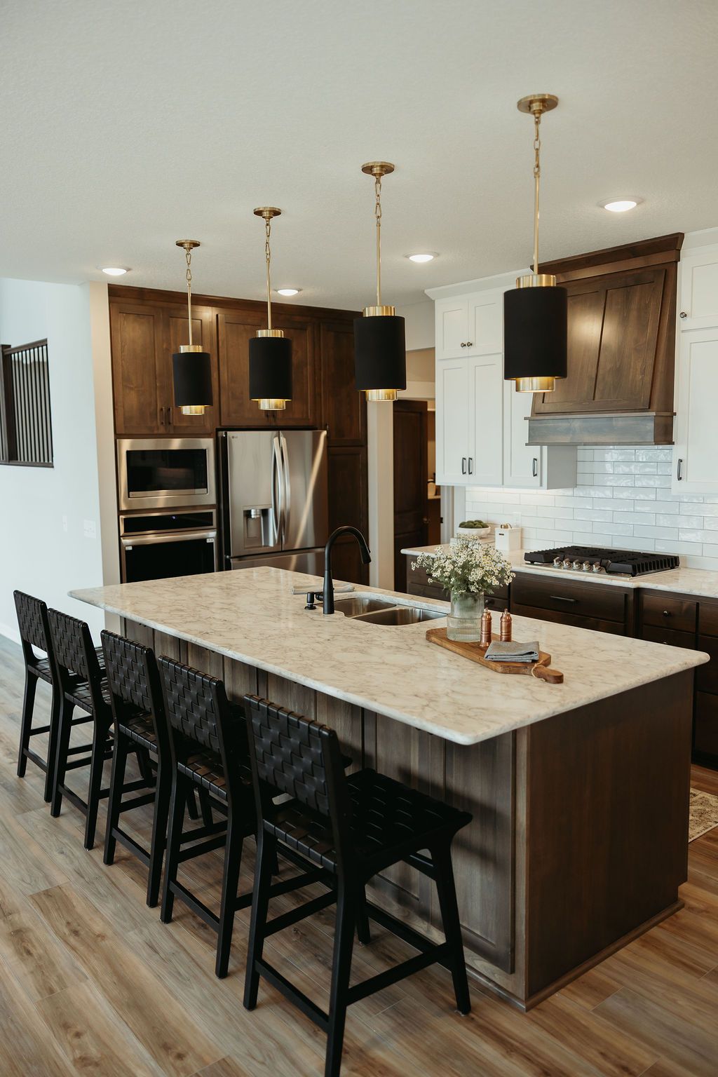 Modern kitchen with island, pendant lights, black bar stools, and dark cabinets.