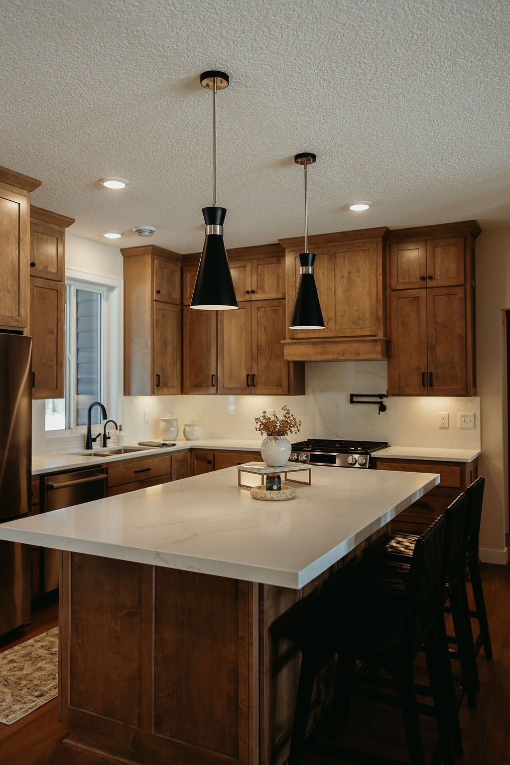 Kitchen with wooden cabinets, white countertops, and black pendant lights.