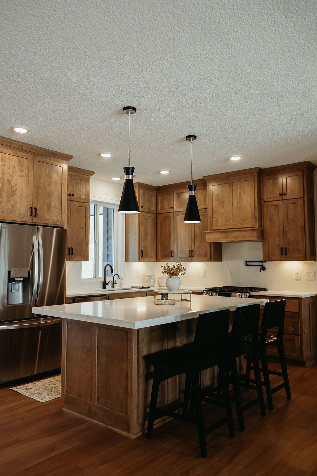Kitchen with wood cabinets, white island countertop, black pendant lights, and stainless steel appliances.