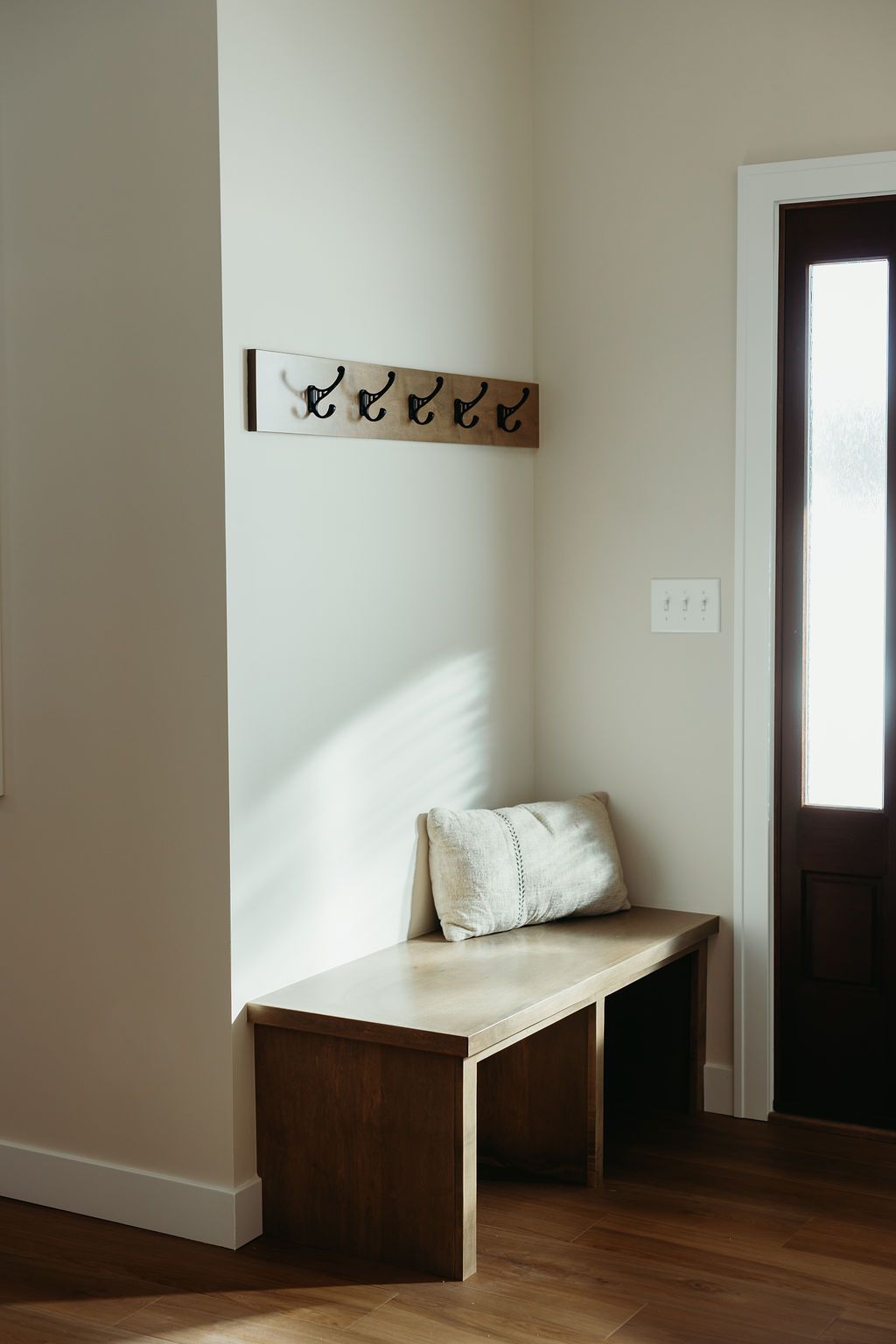 Wooden bench and coat rack in a neutral entryway, with dark door and light walls.
