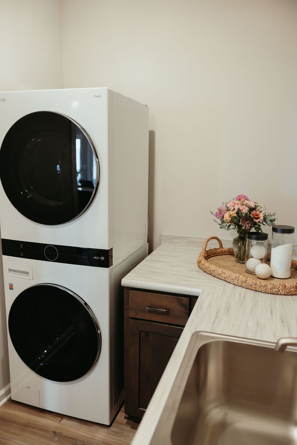 Stacked white LG washer and dryer. Laundry room with countertop, sink, and flowers in a vase.