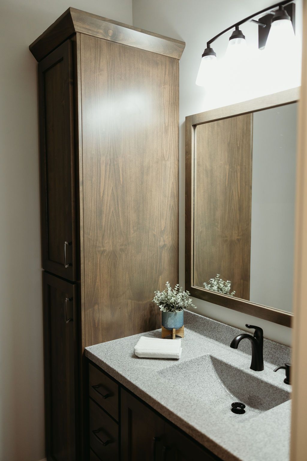 Bathroom with dark wood cabinet, gray countertop, black faucet, and mirror.