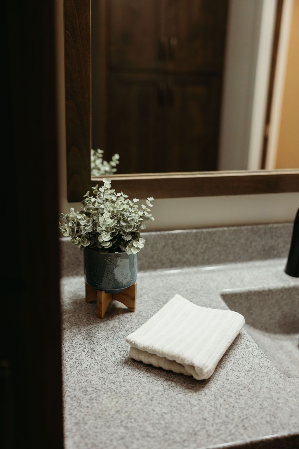 Bathroom counter with a small plant in a blue pot, folded white towel, and mirror.