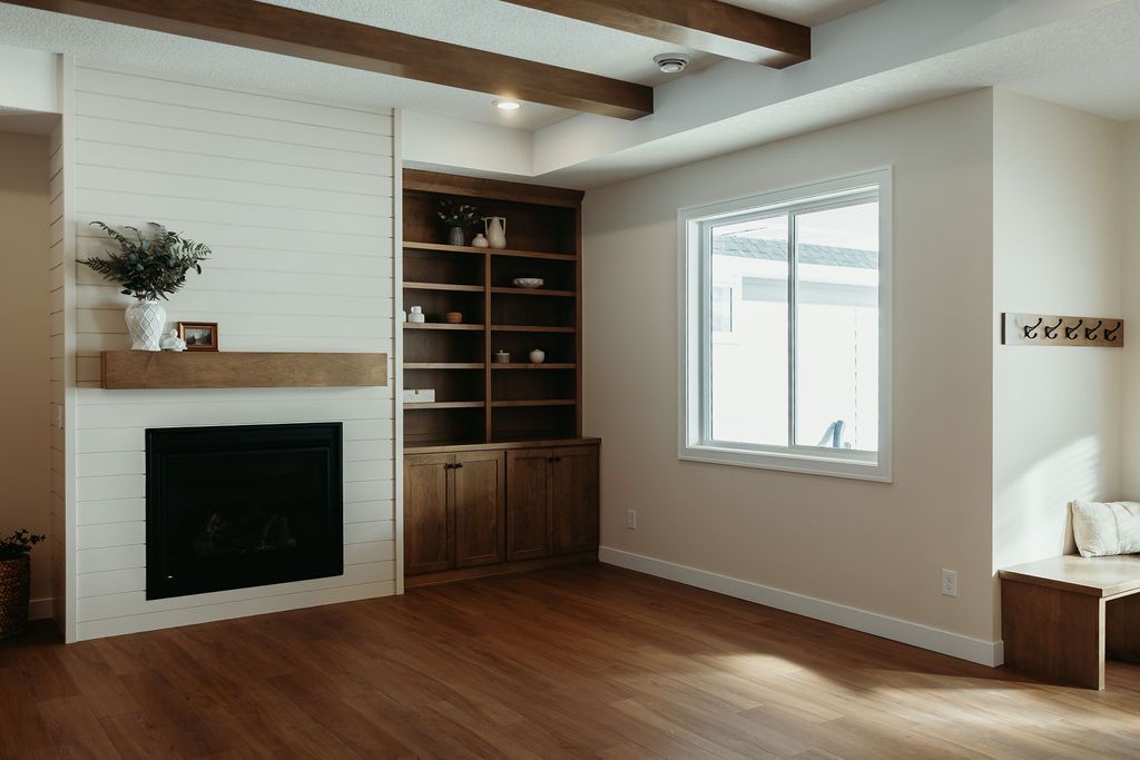 Living room with fireplace, built-in shelving, wood beams, hardwood floors, and a window.