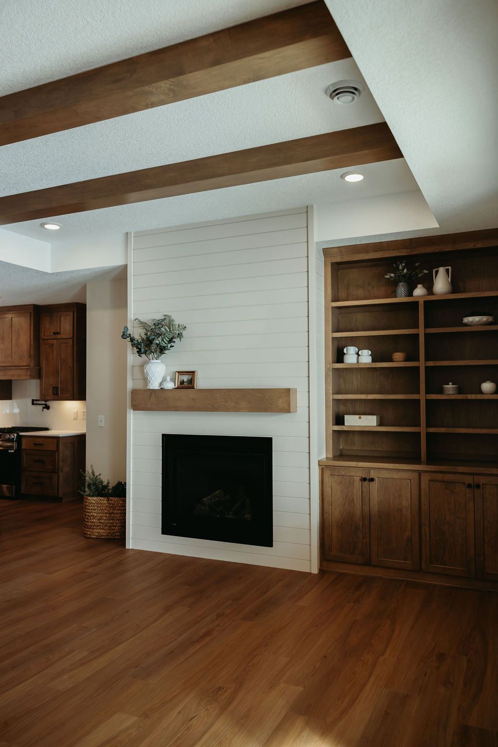 Living room with fireplace, built-in shelving, wooden beams and hardwood floor.