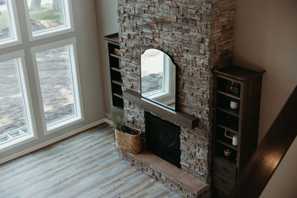 Stone fireplace with mirror and built-in bookshelves, near a large window and wooden floor.
