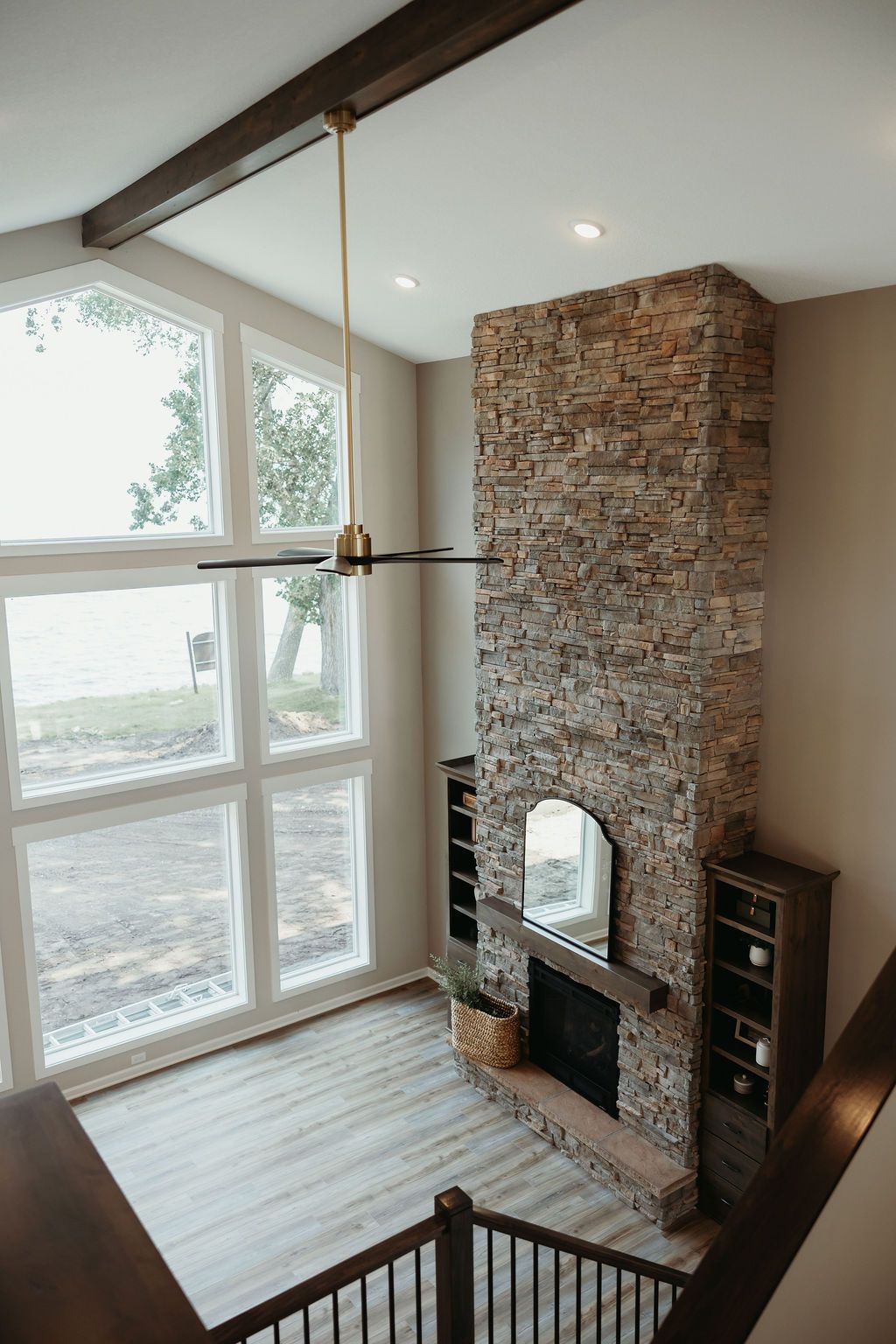 High-angle view of living room with stone fireplace, large windows, and dark wood beams.
