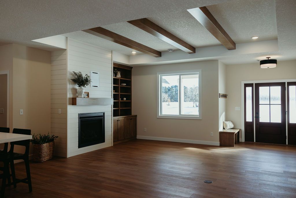 Spacious interior with hardwood floors, fireplace, built-in shelving, and exposed wooden beams on the ceiling.