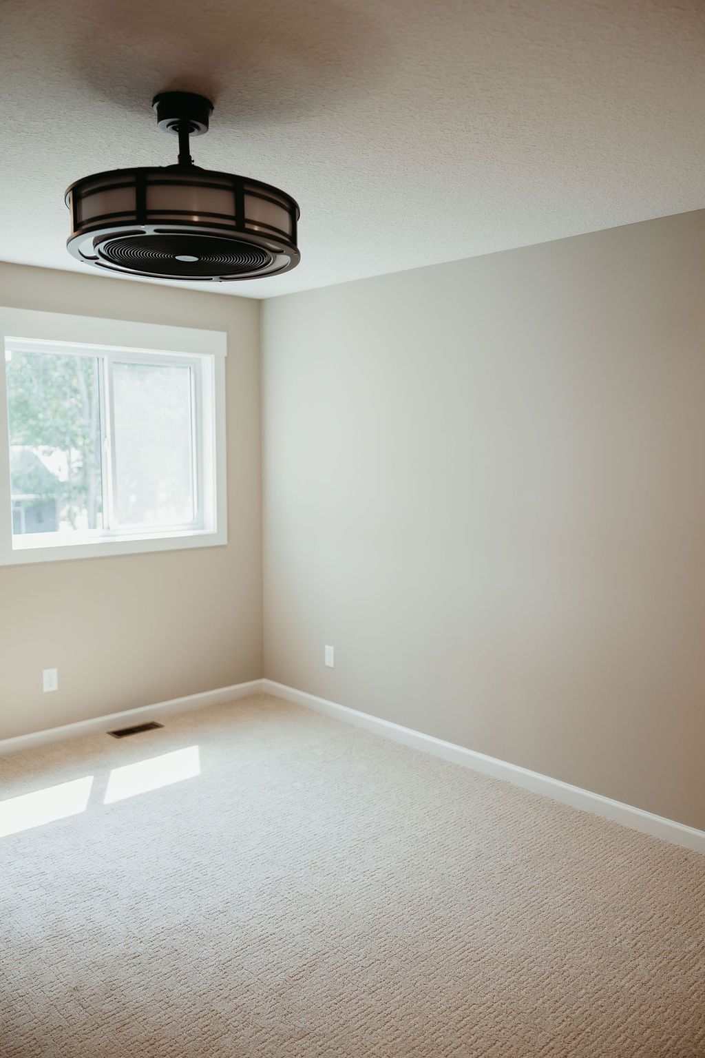Empty room with beige carpet and walls, a window, and a ceiling fan.