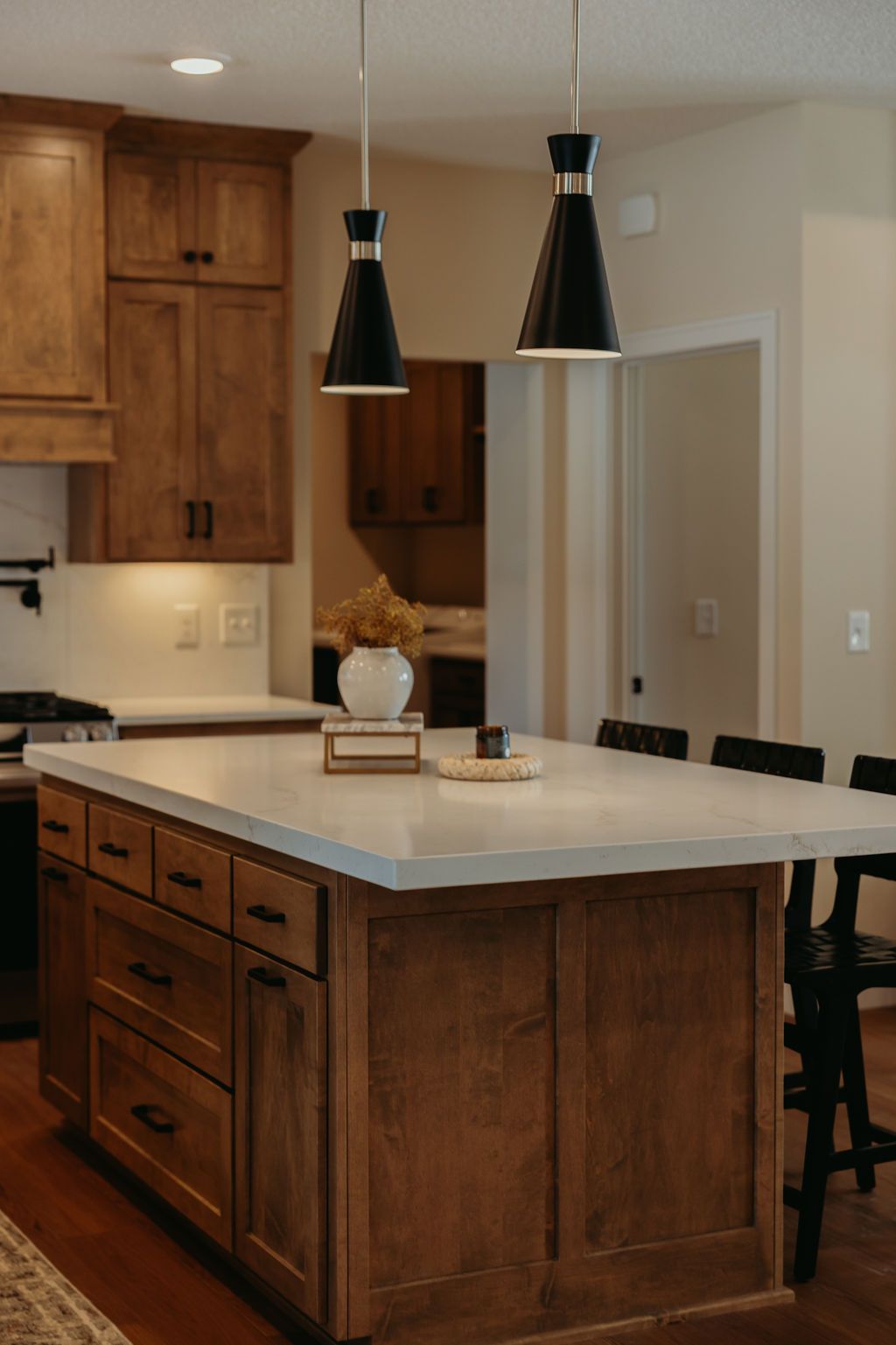 Kitchen island with wooden cabinets, white countertop, black pendant lights, and bar stools.