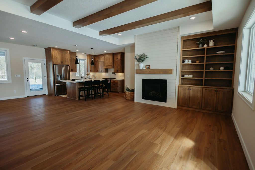 Spacious living area with wooden floors, kitchen, fireplace, and built-in shelves.