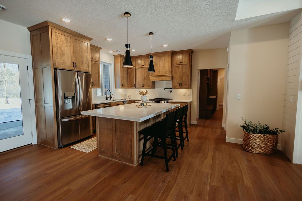 Kitchen with wood cabinets, island with stools, stainless steel fridge, and wooden floors.