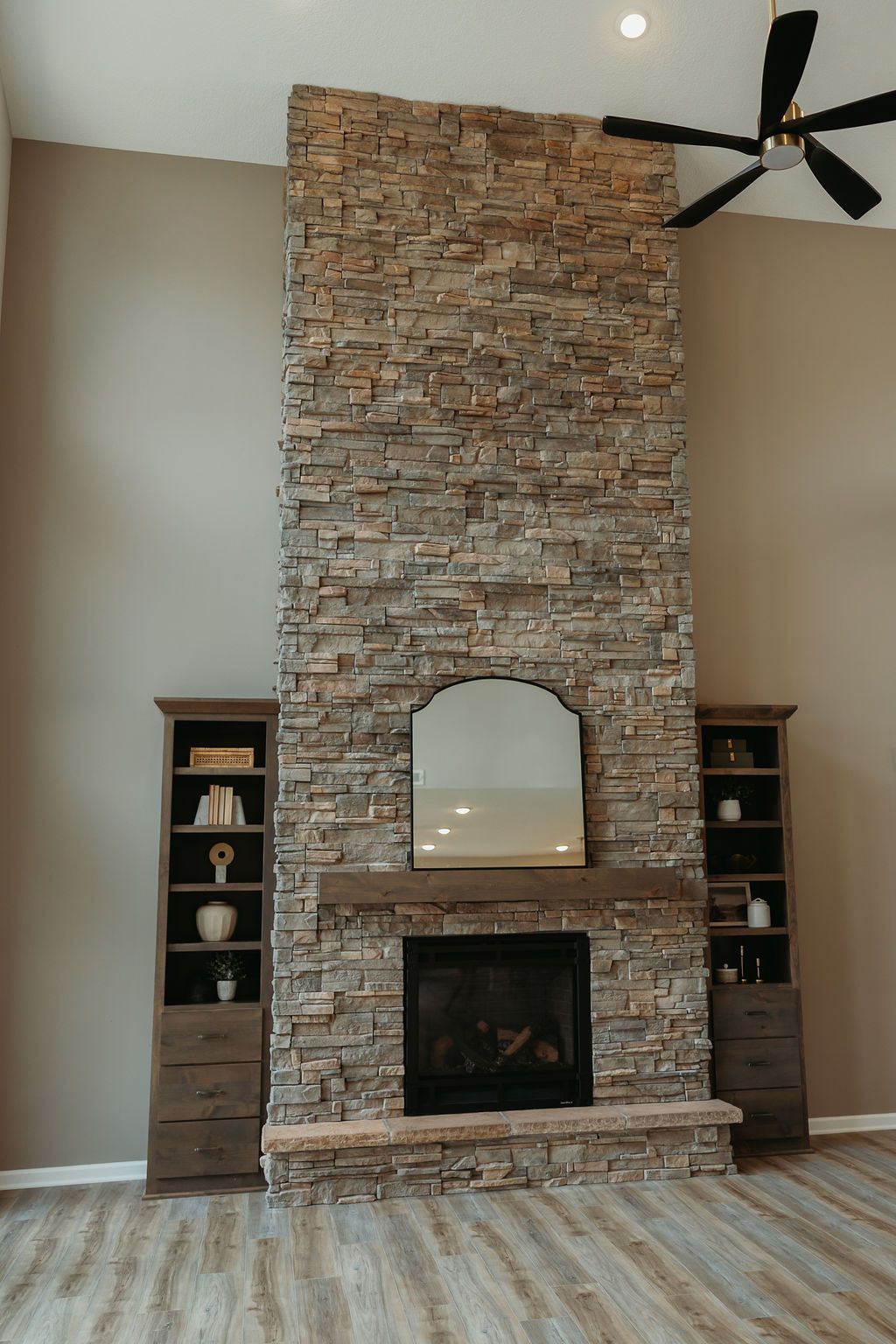 Stone fireplace with mirror, built-in shelving, and wood mantel, in a modern living room.