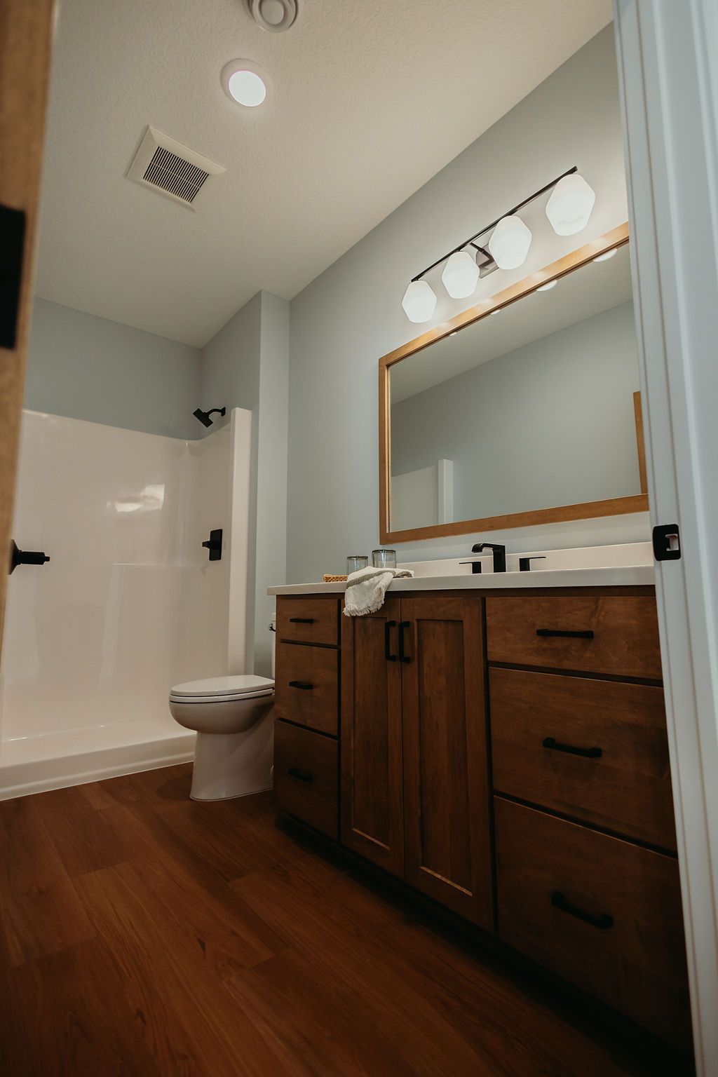 Bathroom with brown vanity, wood floor, white shower, and light blue walls.