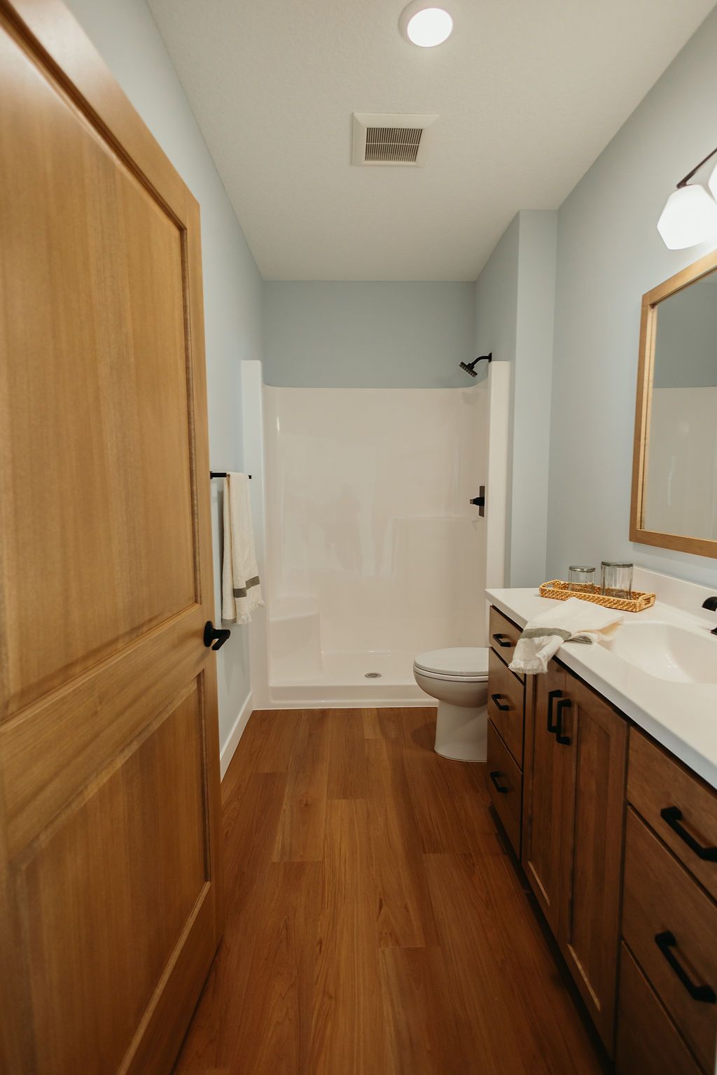 Bathroom with light wood floor, blue walls, a white shower, and wood vanity with white countertop.