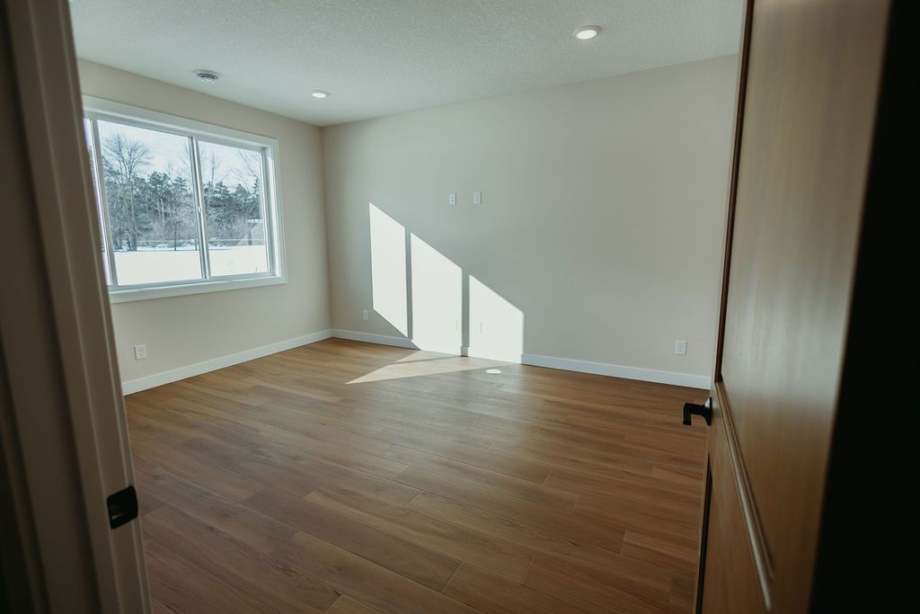 Empty room with hardwood floors, a window with sunlight, and a partially open door.