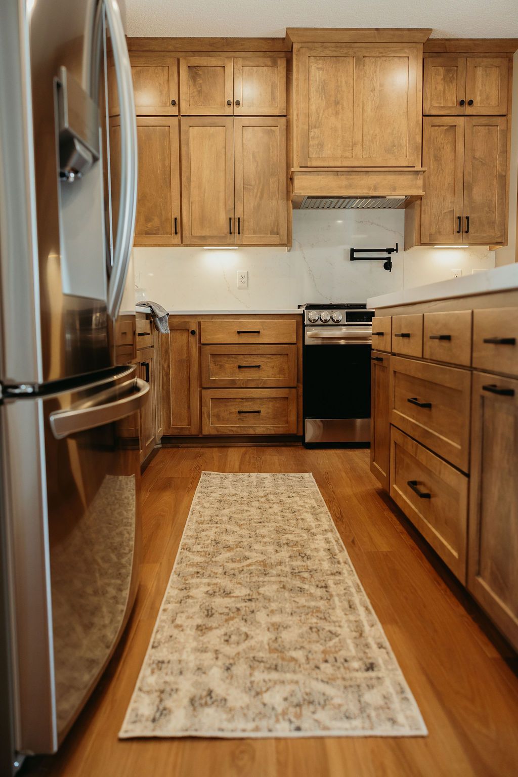 Kitchen with light wood cabinets, stainless steel appliances, and a patterned runner rug.
