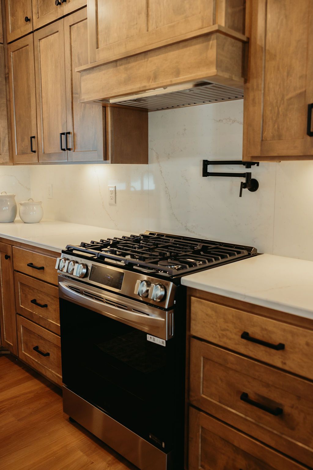 Kitchen with light-brown cabinets, stainless steel stove, white countertops, and black hardware.