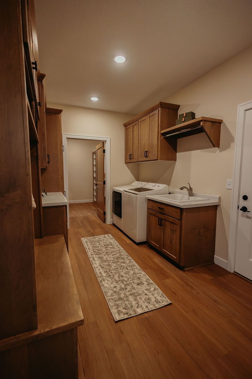 Laundry room with wooden cabinets, washer/dryer, sink, and hardwood floor. Doorways lead to adjacent rooms.
