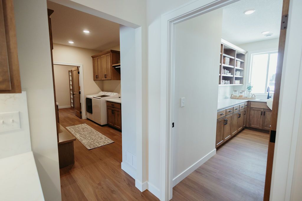 View of a kitchen doorway leading to a laundry room and pantry with wooden cabinets and hardwood floors.