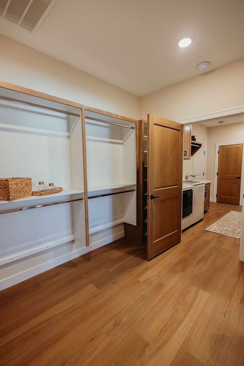Wooden-floored pantry with shelves and open door to laundry area with appliances and another door.