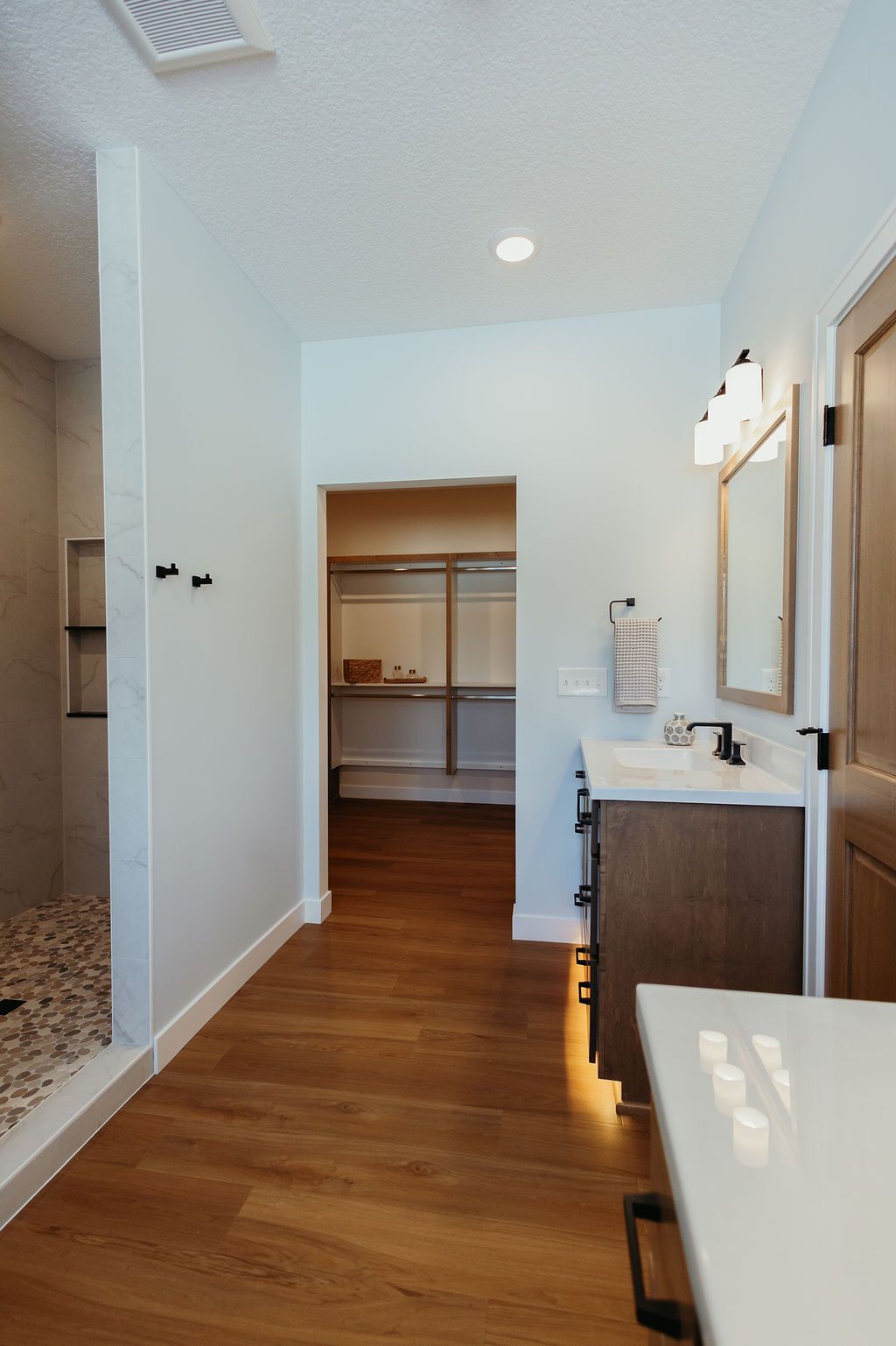 Bathroom with shower, vanity, and walk-in closet, brown wood flooring, light blue walls, and white countertop.