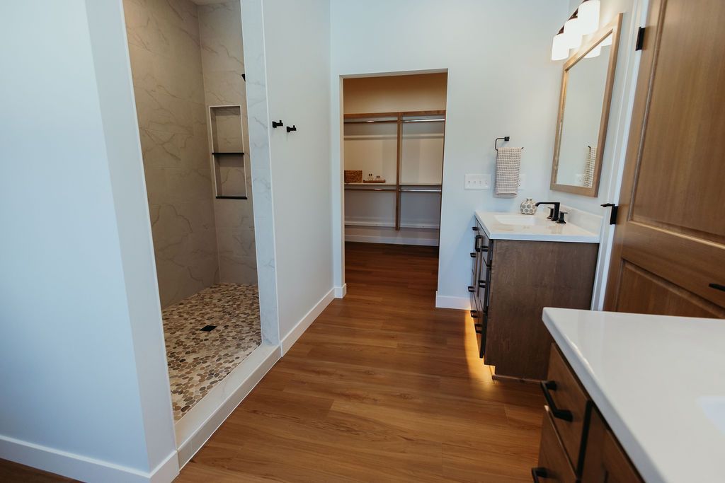 Bathroom with walk-in shower, vanity, and walk-in closet. Hardwood floors and neutral walls.