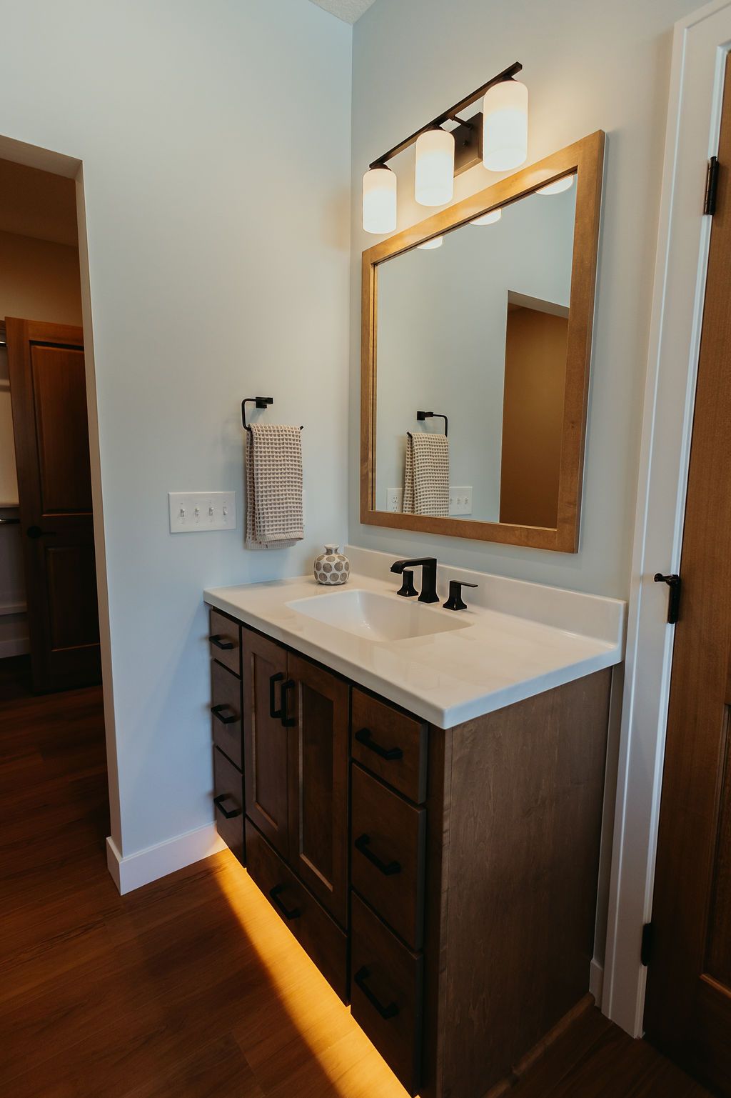 Bathroom with a wooden vanity, mirror, and light fixture; blue walls, hardwood floor.
